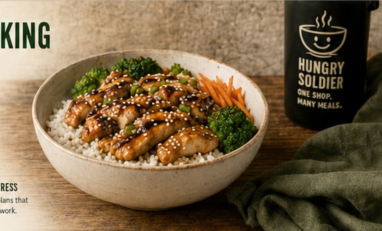 A bowl of teriyaki-style chicken, rice and vegetables beside a Hungry Soldier mug